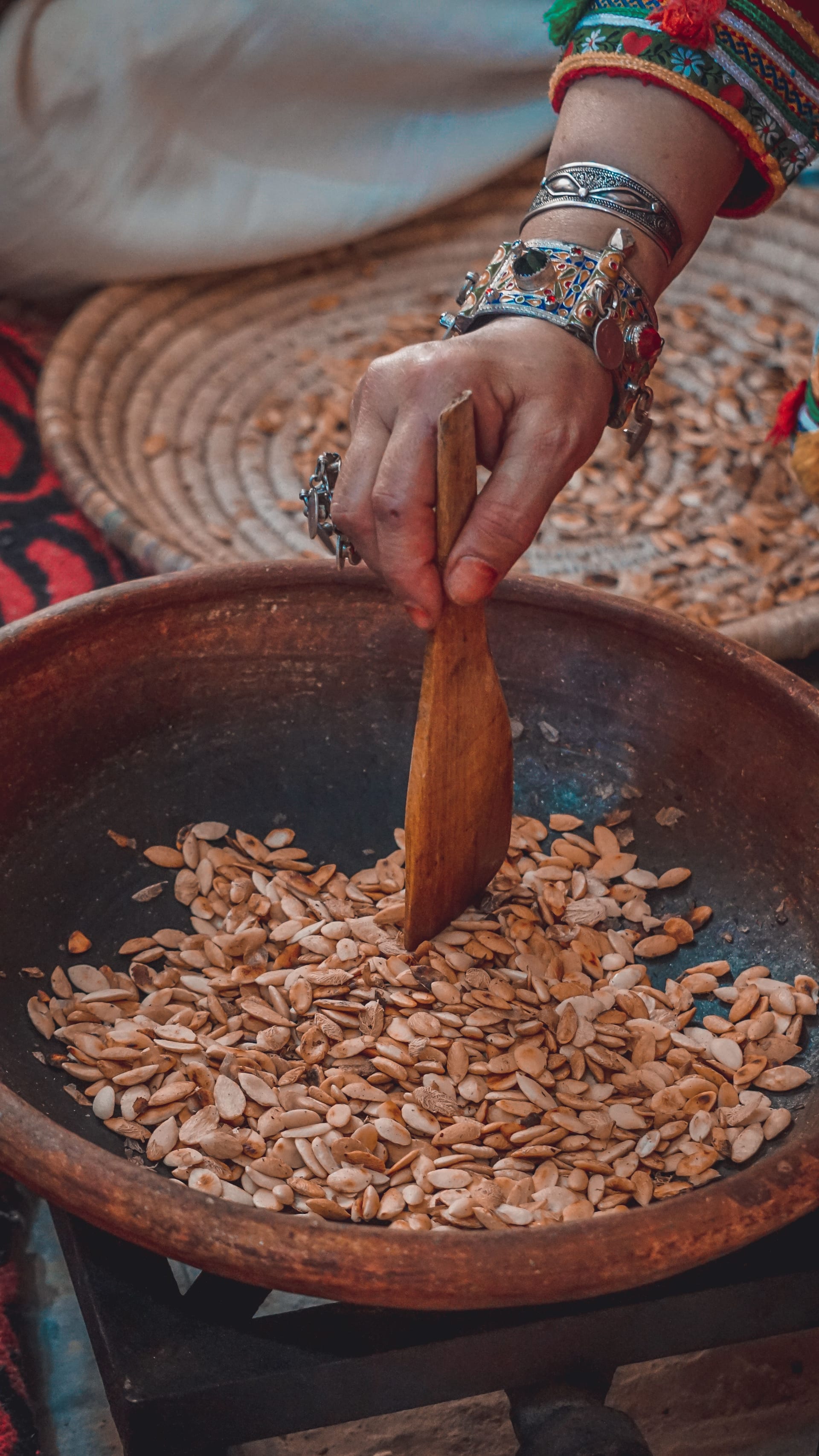 Moroccan woman in traditional dress toasting argan kernels in a clay bowl